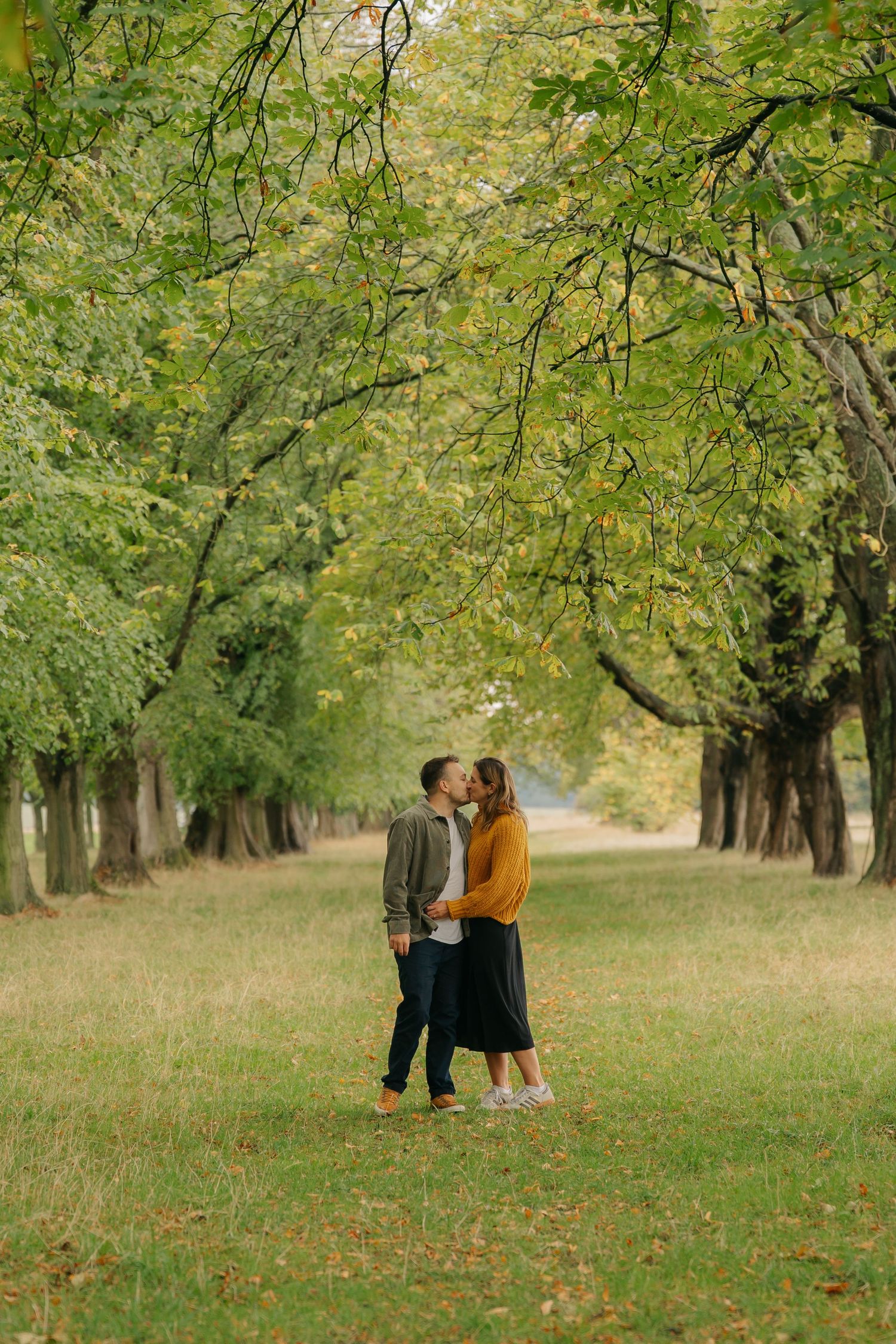 A couple shares a playful moment together in a grassy field with rustic brick ruins in the background.