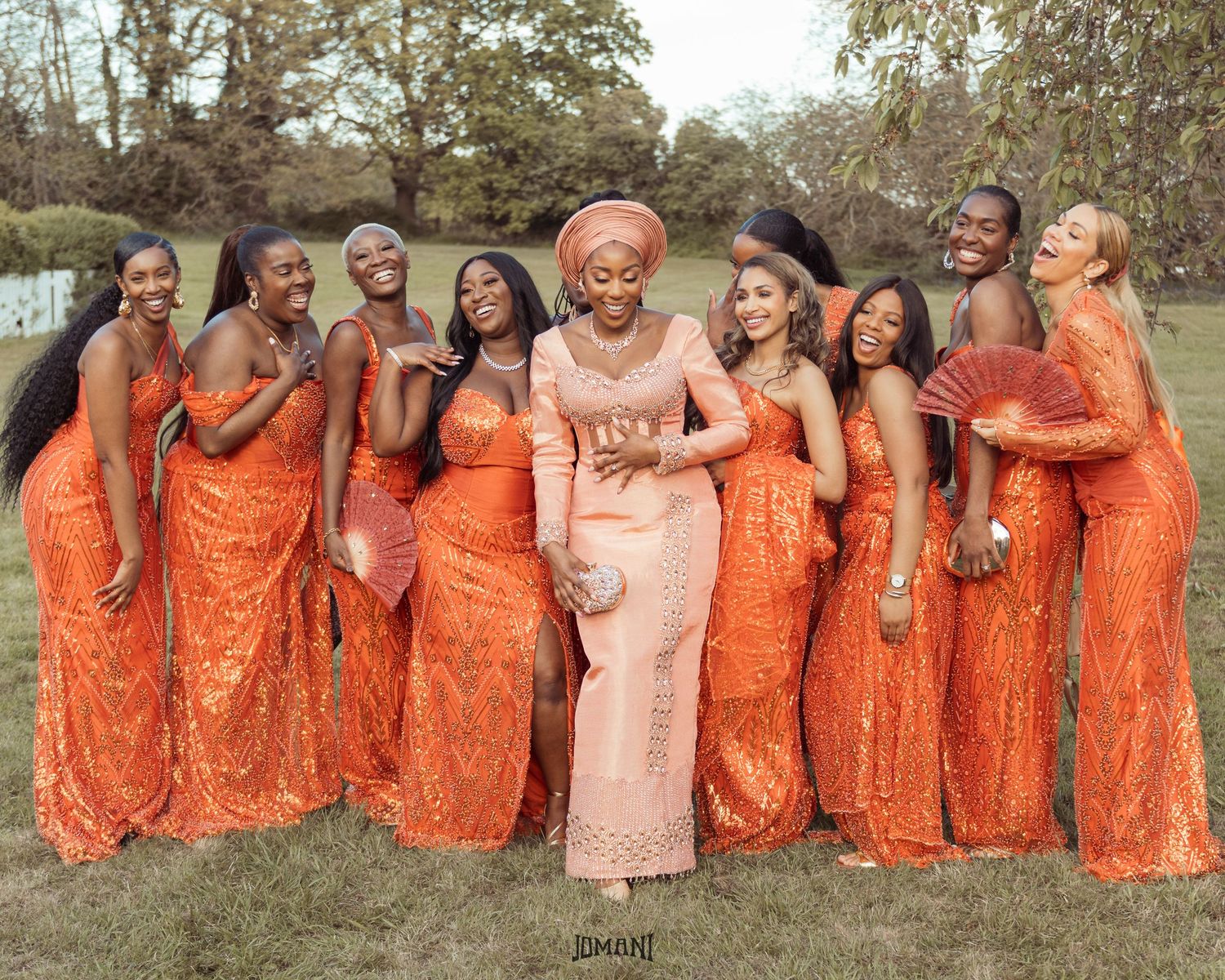 Group of bridesmaids in matching orange sequin gowns posing outdoors with bride in peach Nigerian traditional attire.