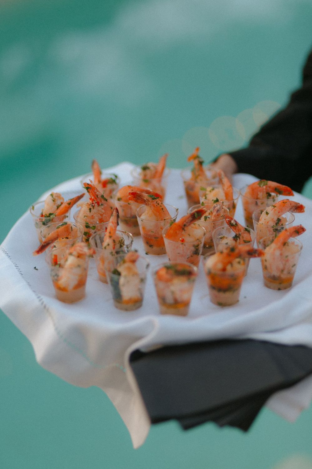 Grilled shrimp appetizers arranged in a row on a white serving platter against a teal background.