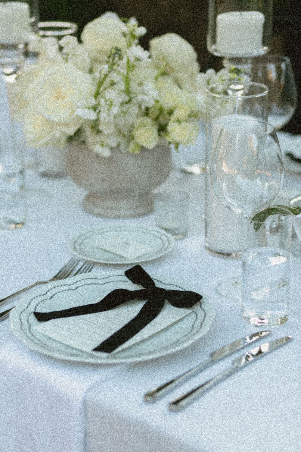 Elegant white table setting with black napkins and crystal glassware on a crisp white tablecloth with floral accents.