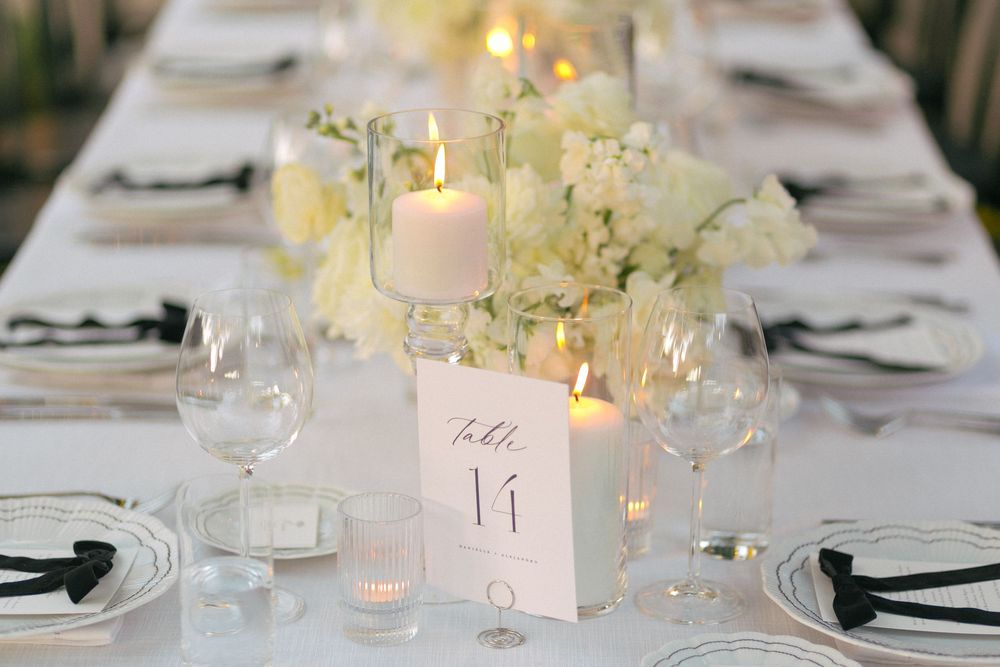 Elegant white wedding table setting with glowing candles, hydrangeas, and table number in soft romantic lighting.