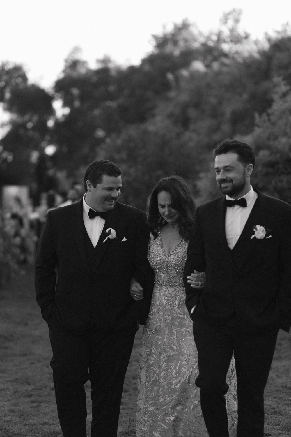 Wedding party in formal attire walks and laughs together outdoors in black and white photograph.
