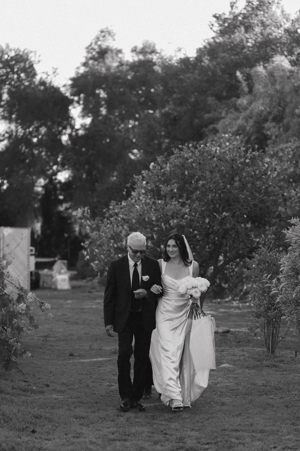 Black and white wedding photo series showing couple walking through an orchard on their special day.