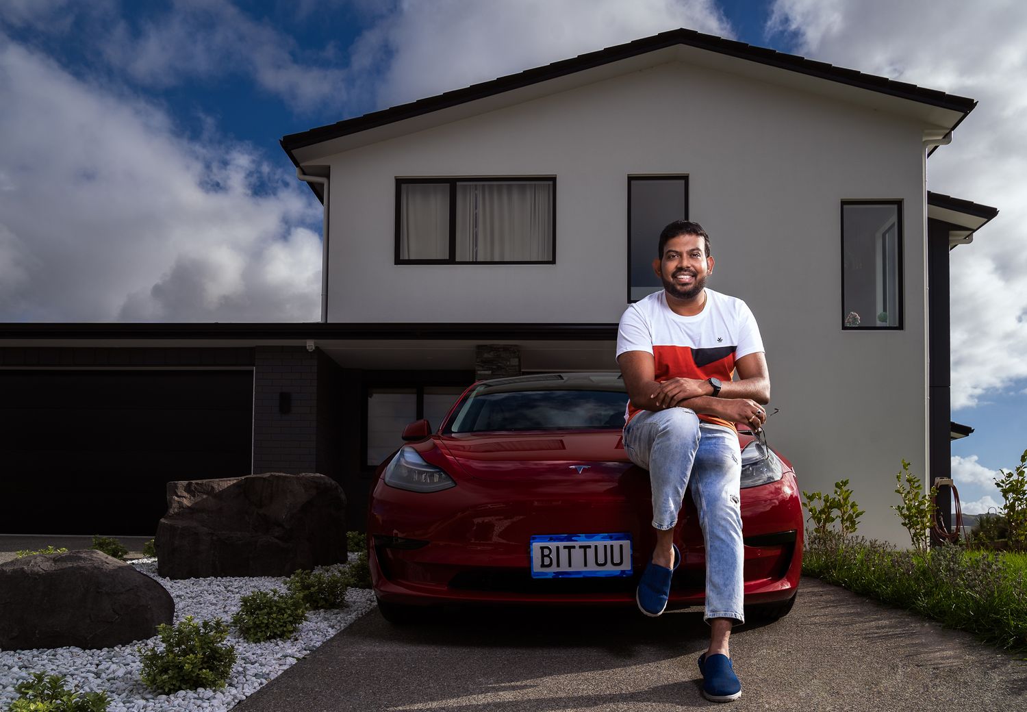 Modern white house exterior with red car parked in driveway under cloudy sky.