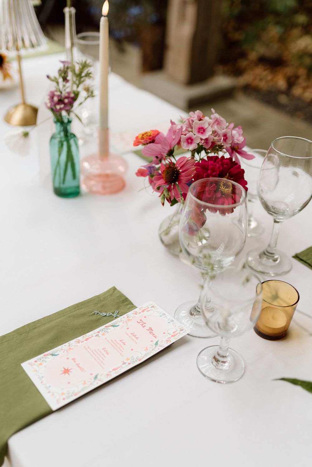 the table scape featuring hand made napkins, florals, candles, and coloured glass for vases and tea lights.