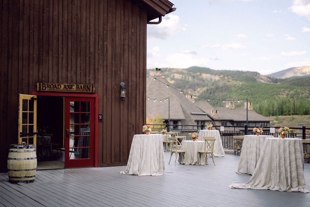 Rustic wooden barn venue decorated with elegant cream tablecloths and wine barrels against a scenic mountain backdrop.