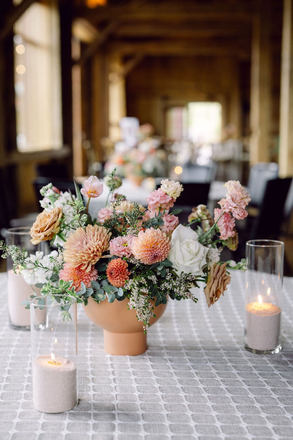 Elegant table centerpiece with peach dahlias, pink roses, and greenery in concrete vessels with glowing candles.