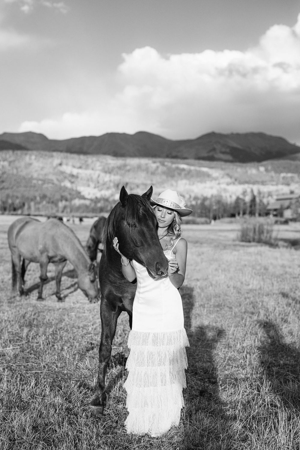A black and white photo series showing a horse standing next to a white wedding dress in a mountain meadow field.