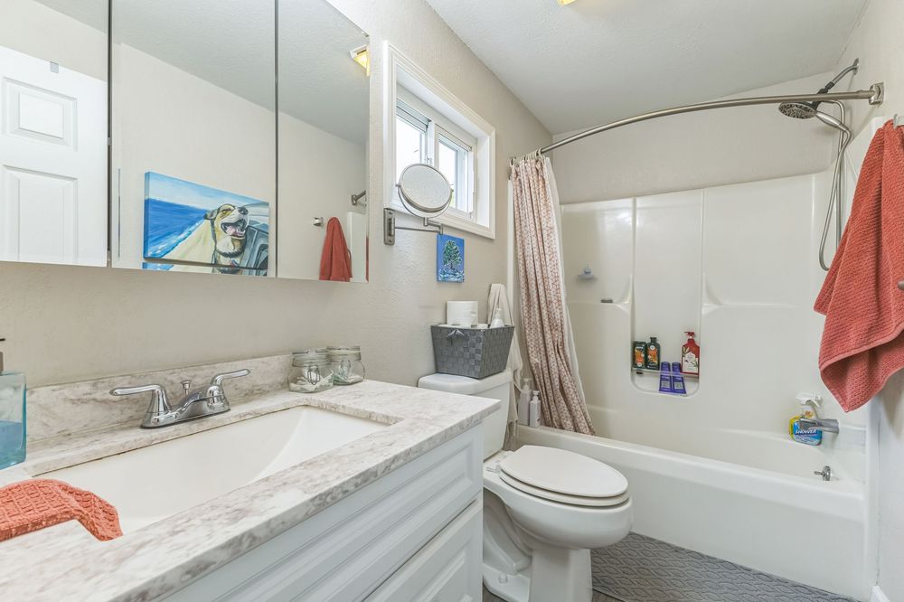 Clean full bathroom with marble vanity, toilet, shower-tub combo with curtain, and large mirror.