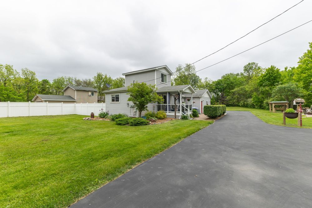 Single-family home with gray siding, manicured lawn, paved driveway, covered porch, and lush surrounding trees.