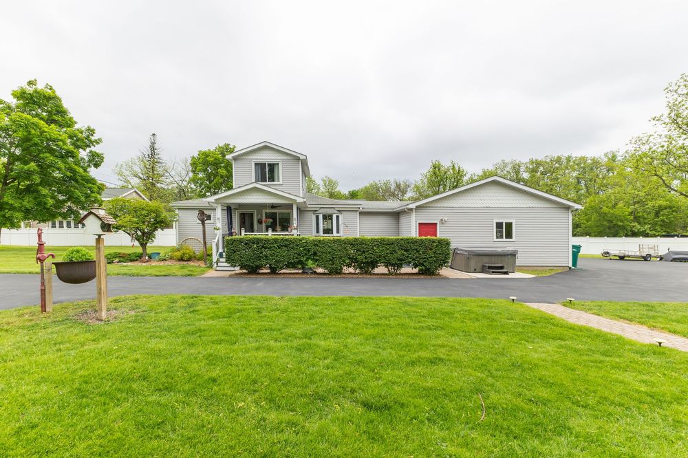 Ranch-style home with gray siding, large green lawn, paved circular driveway, attached garage, and mature trees.