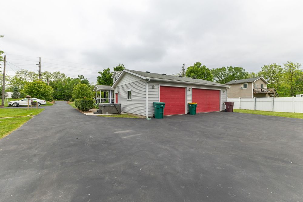 Detached two-car garage with red doors, gray siding, large paved driveway, and white privacy fence.