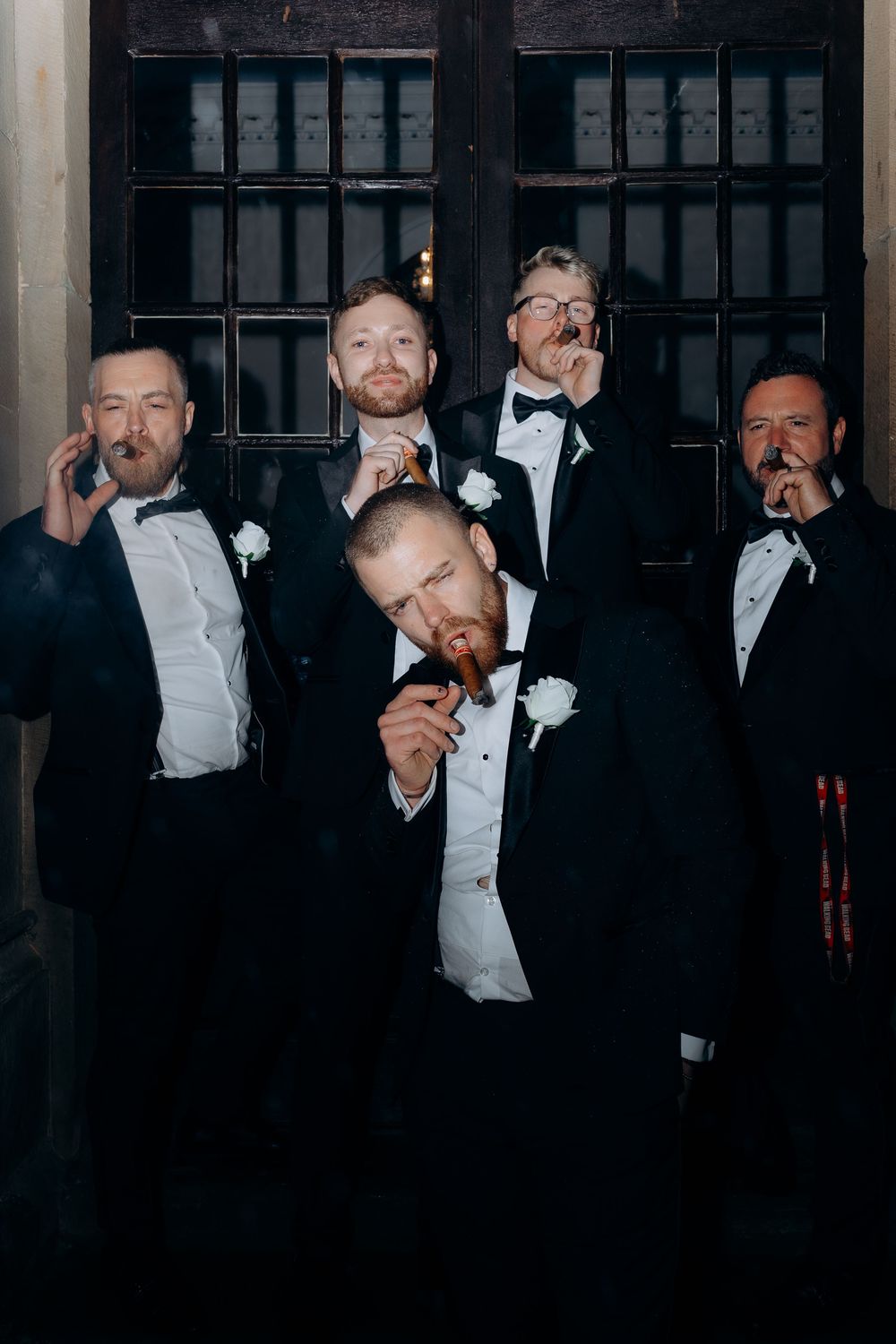 Groomsmen in black tuxedos and bow ties share laughs during formal wedding photos.