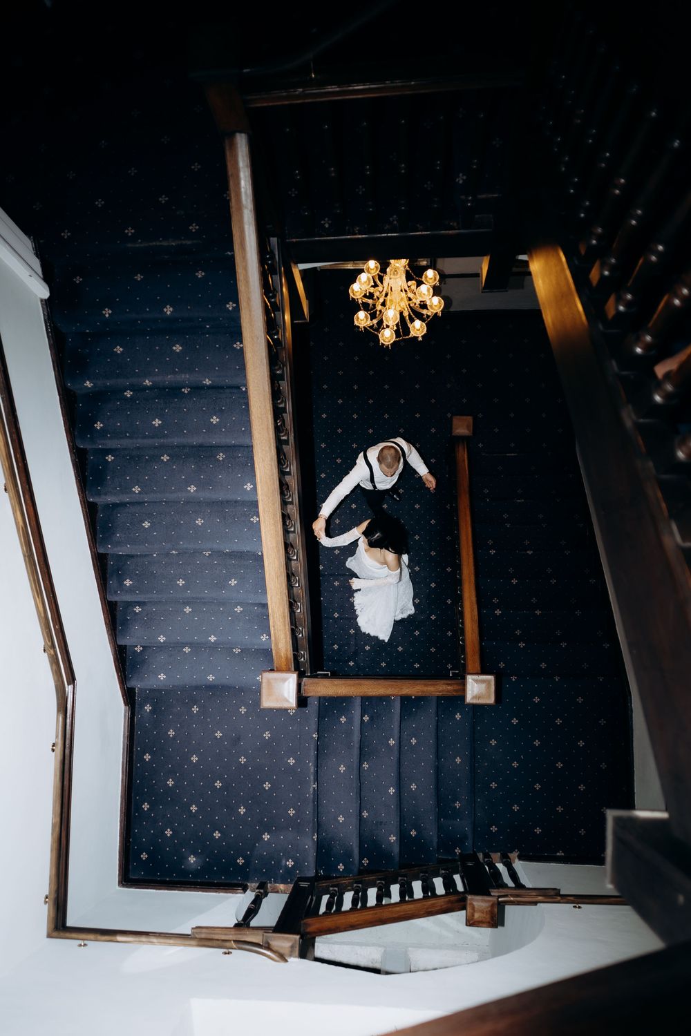An empty hotel hallway with patterned carpet and wall sconces creating dramatic lighting.