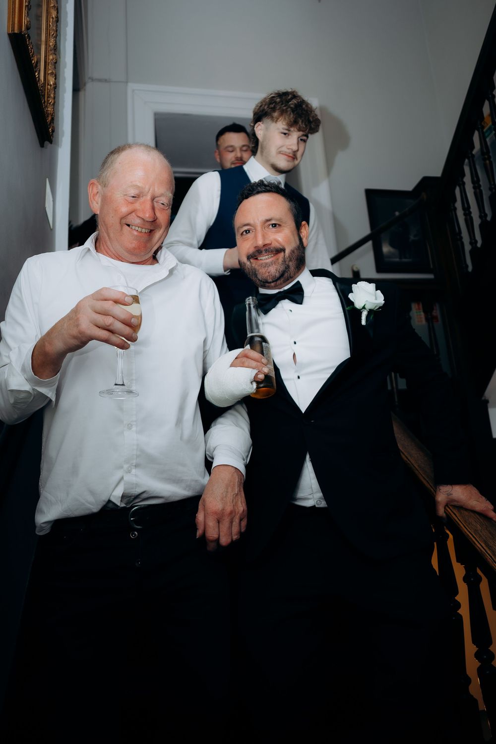 A group in formal white dress shirts and black vests share drinks and laughter at what appears to be a celebration.