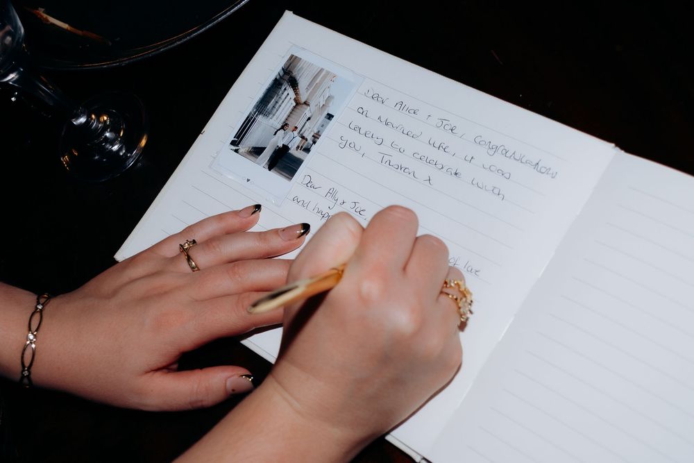 Close-up of hands writing with a pen on white paper while wearing rings.