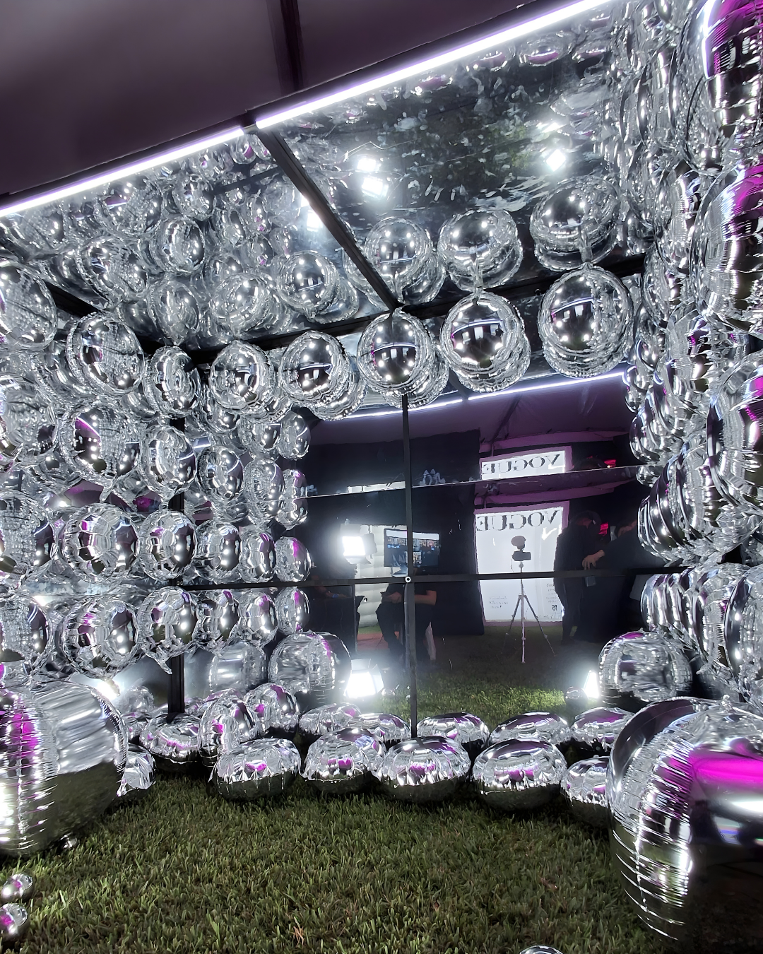 Illuminated bubble-like spheres create a mesmerizing ceiling display at an indoor venue with grass flooring.