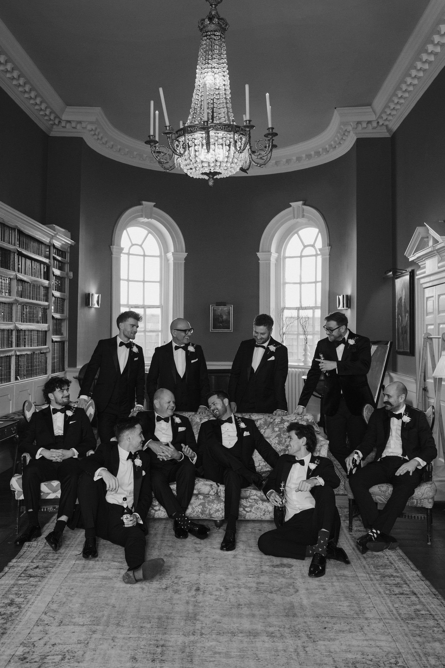 groomsmen sitting on sofa chatting and laughing with whiskey in hand in the library at Iscoyd park