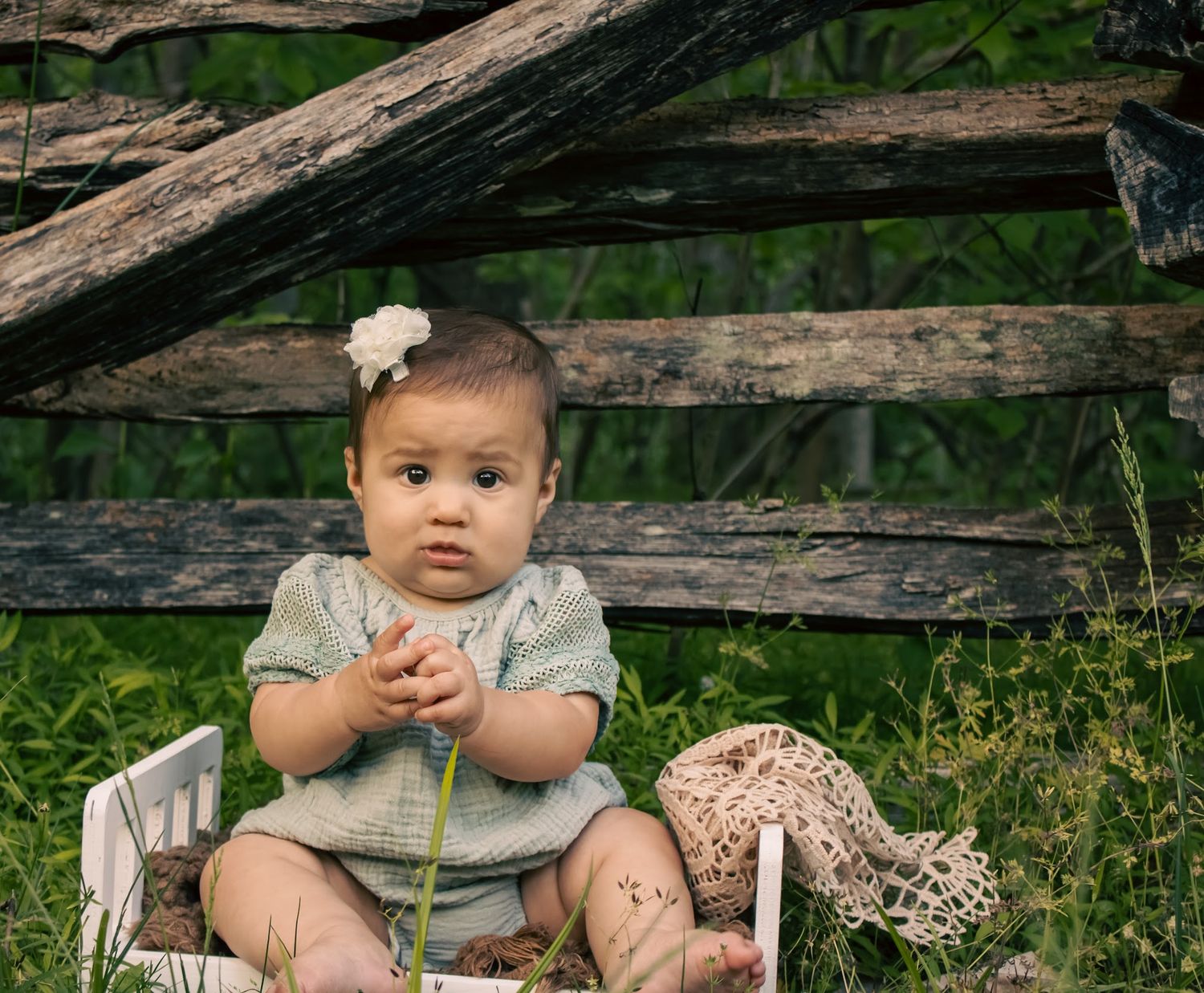 baby girl holding hands wearing a safe green romper in front of wooden fence in yorktown virginia