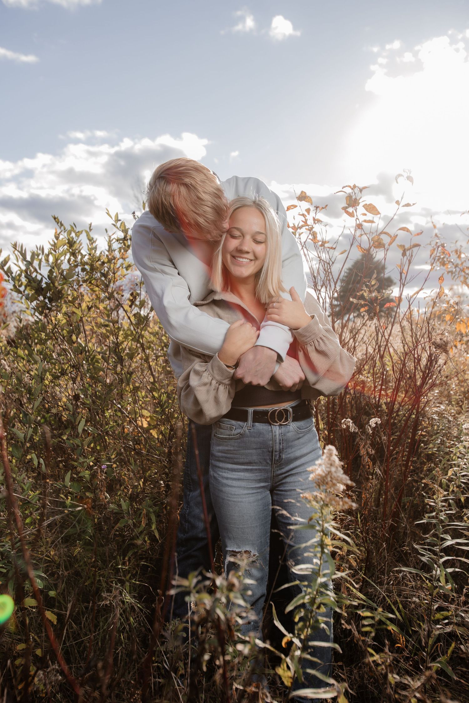 Romantic couple embracing in tall grass field during golden sunset.