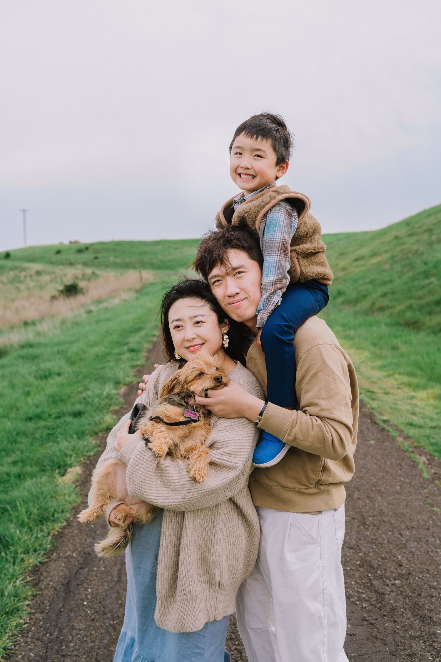 A family and their small dog share joyful moments together on a grassy hillside path.