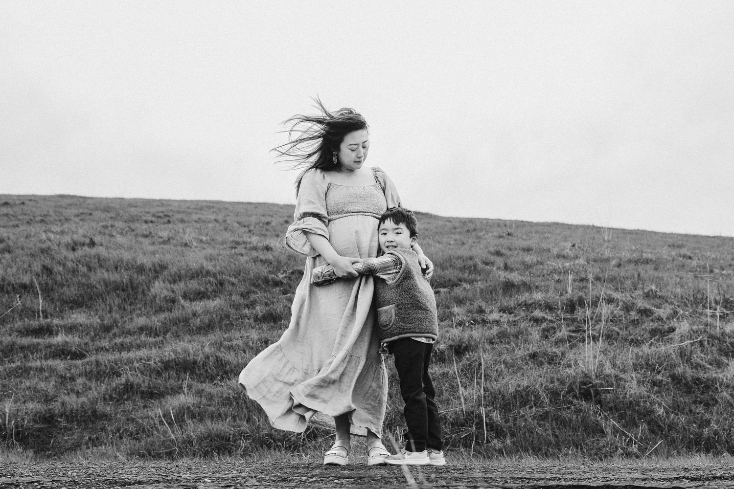 A person in a flowing dress dances and twirls gracefully across a windswept grassy hillside in black and white.