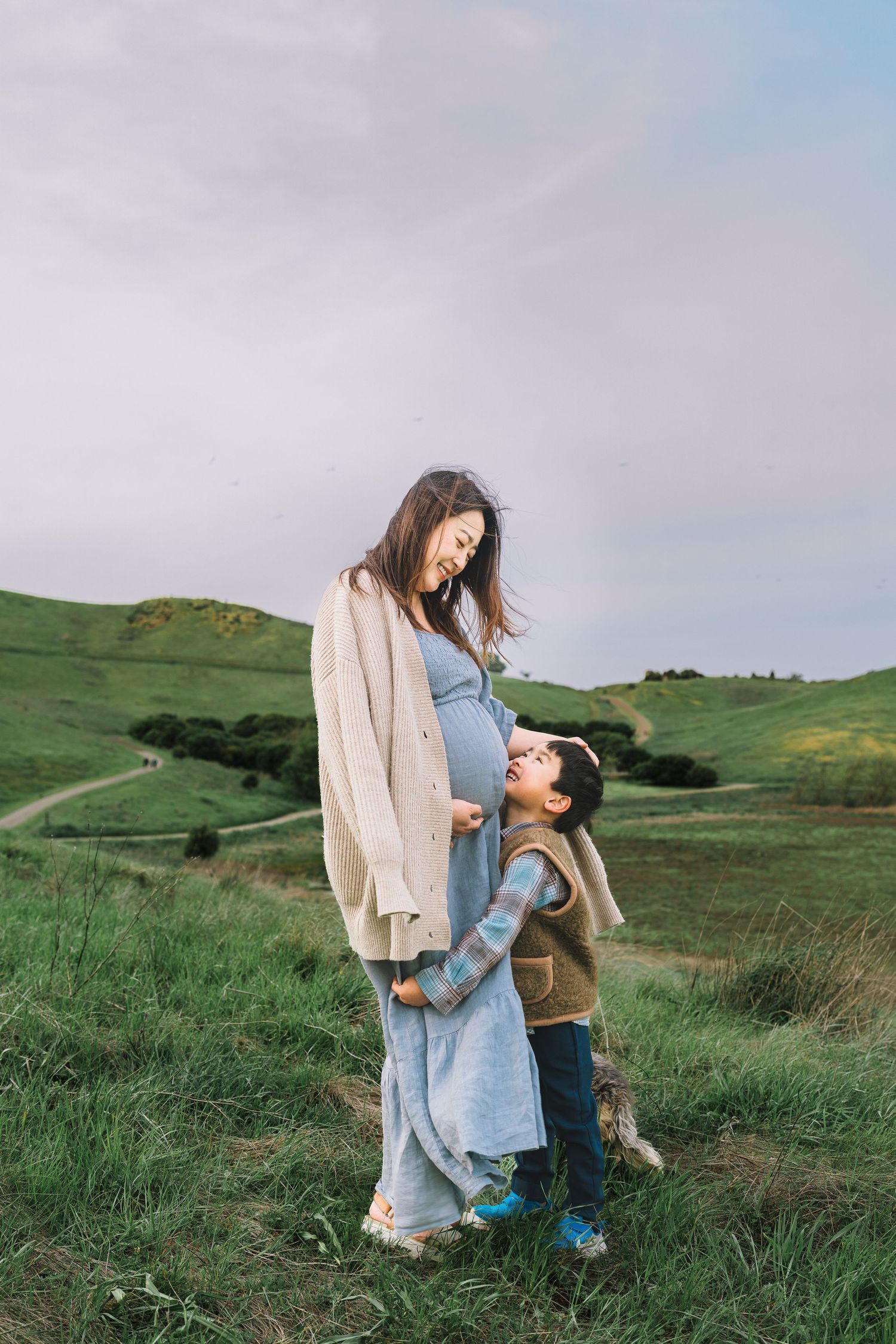 A parent and child share a tender moment while walking together on a green hillside at sunset.