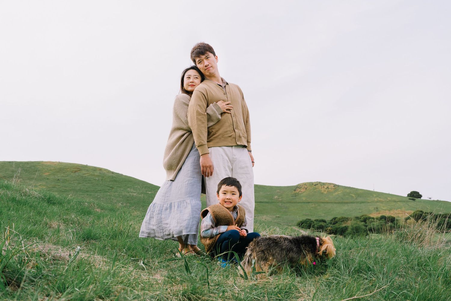 People sit and relax together on a grassy hillside overlooking a scenic rural landscape during golden hour.