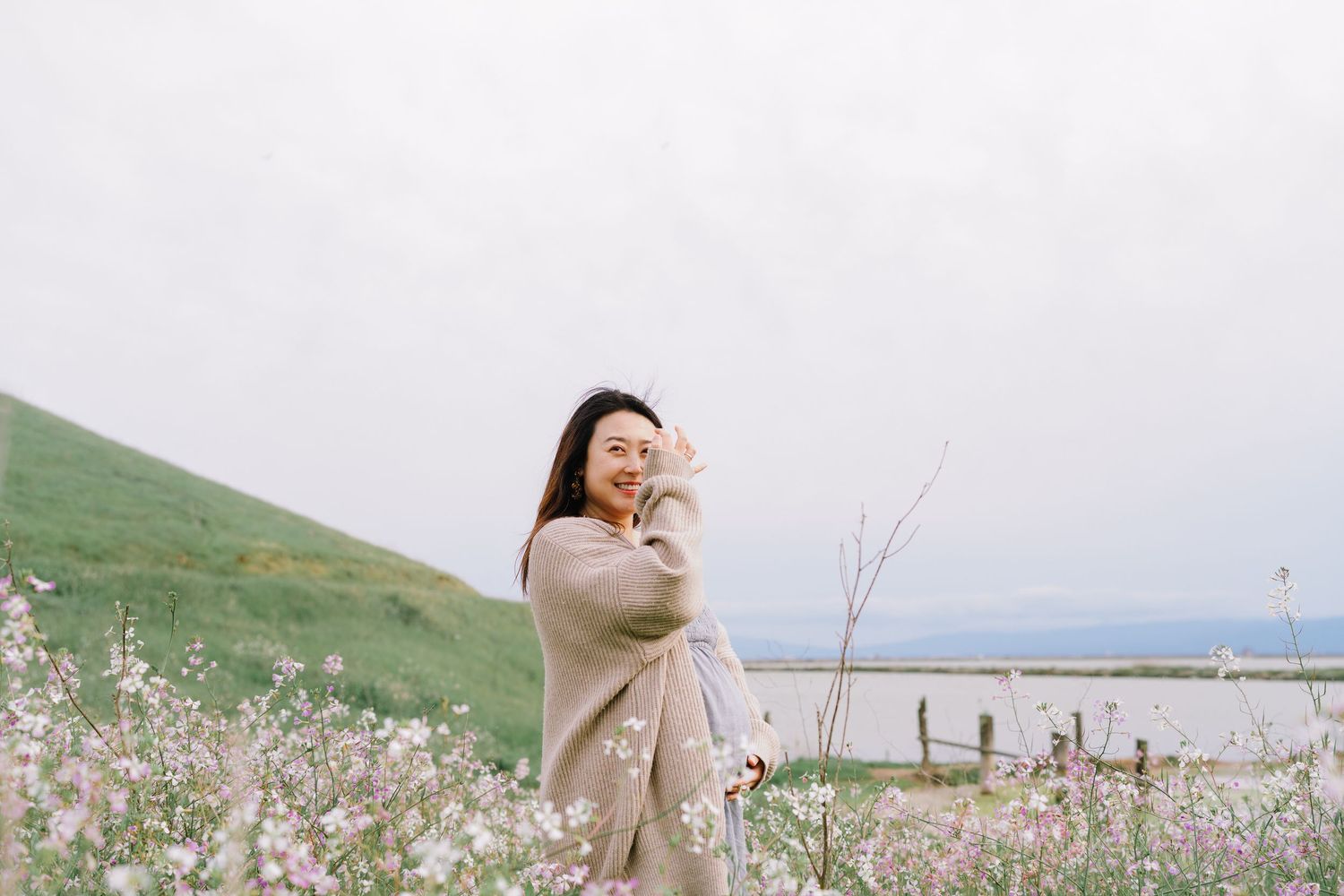 Person in beige coat enjoying a scenic coastal view with blooming flowers in the foreground.
