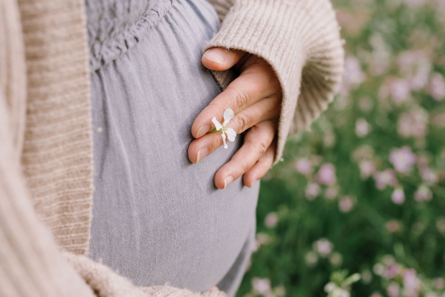 A hand wearing a silver ring holds a delicate cream-colored knit blanket with tassels and fringe details.