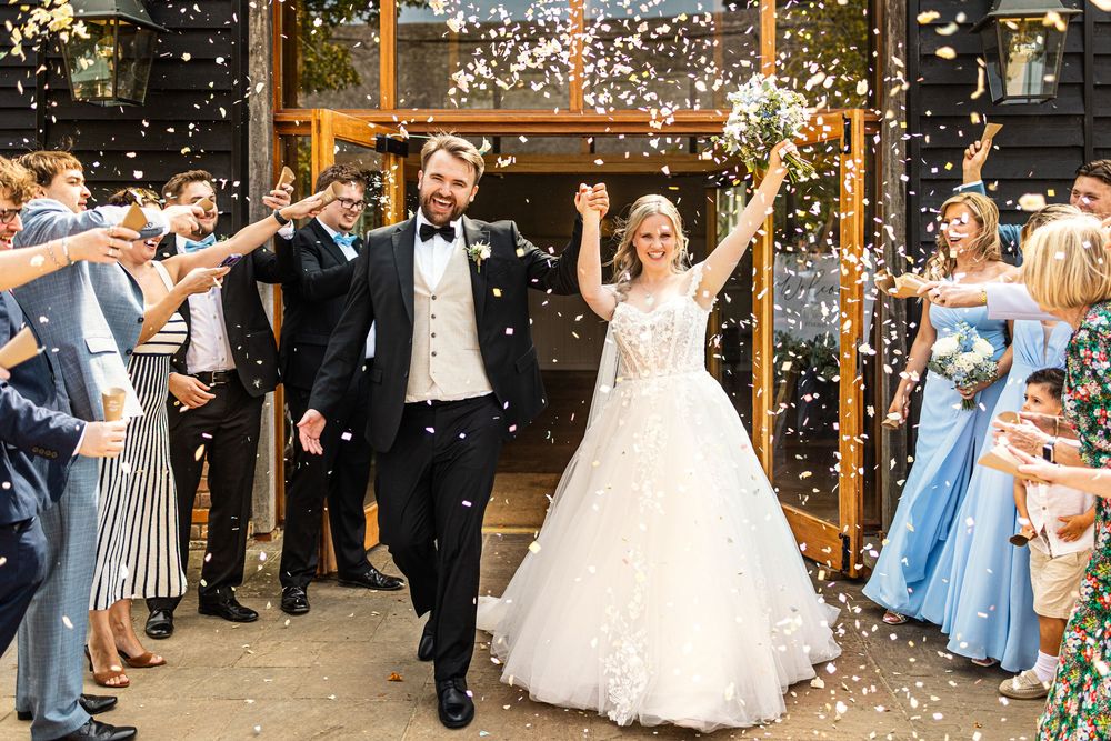 Newlyweds celebrate with raised arms as guests shower them with confetti outside elegant wedding venue doors.