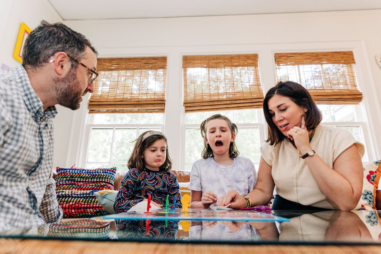 A family sits around a table playing together a game of Candy Land spread laid out in front of them.