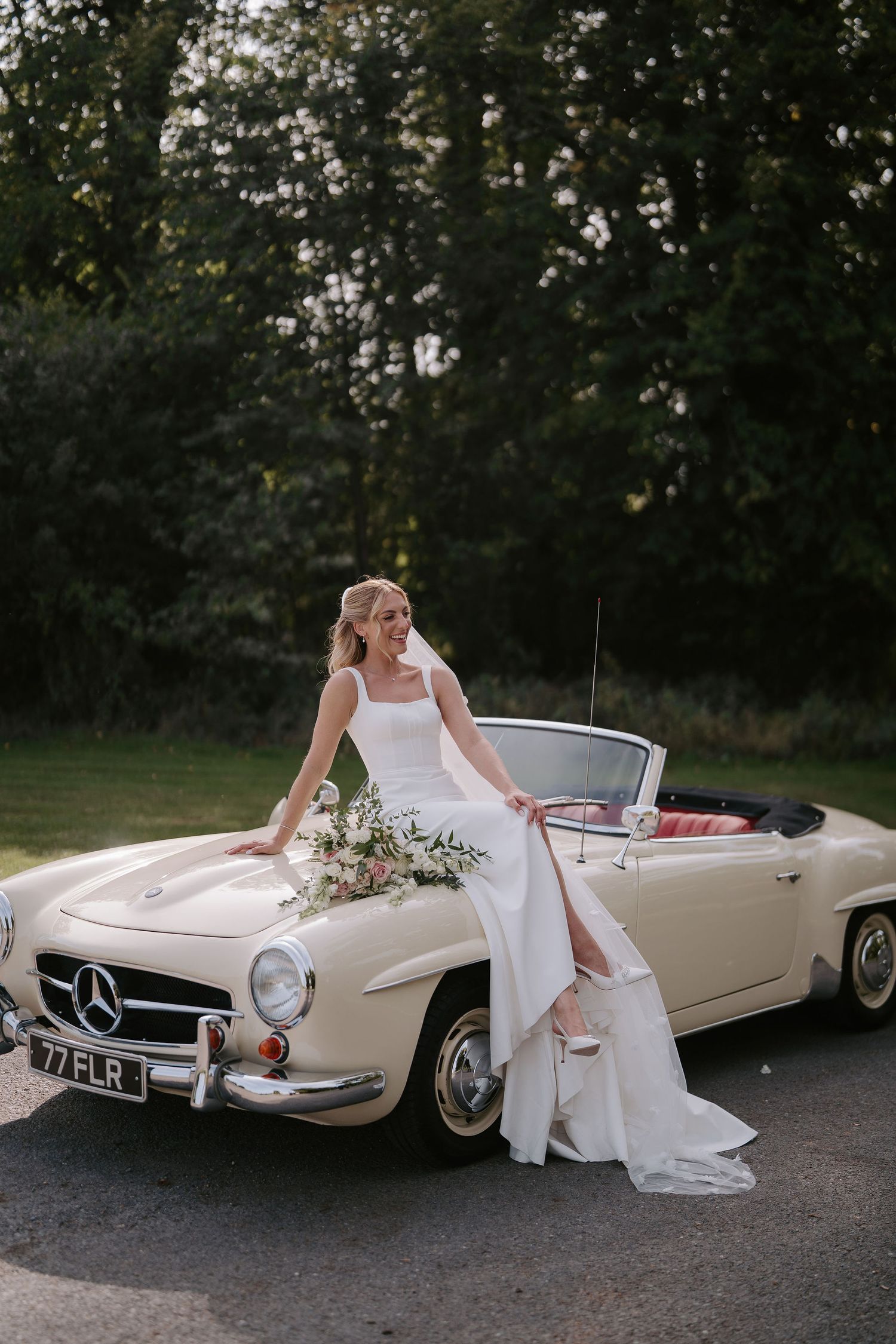 bride sitting on wedding car bonnet at ivy lodge in cirencester