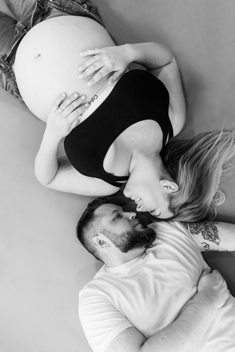 Black and white maternity photo of couple lying together with pregnant belly in focus.