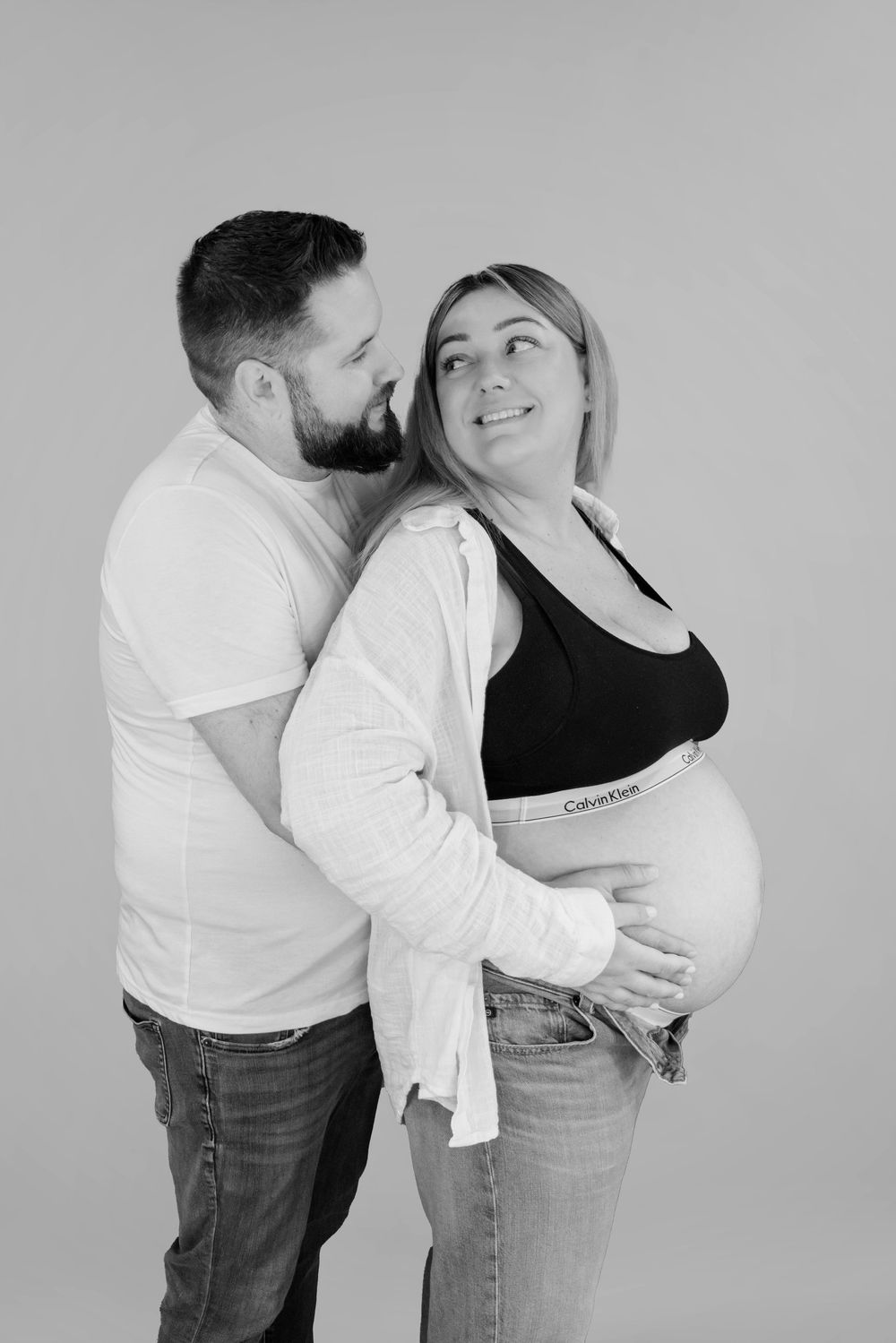 Black and white maternity photo series showing couple embracing and kissing during pregnancy photoshoot.