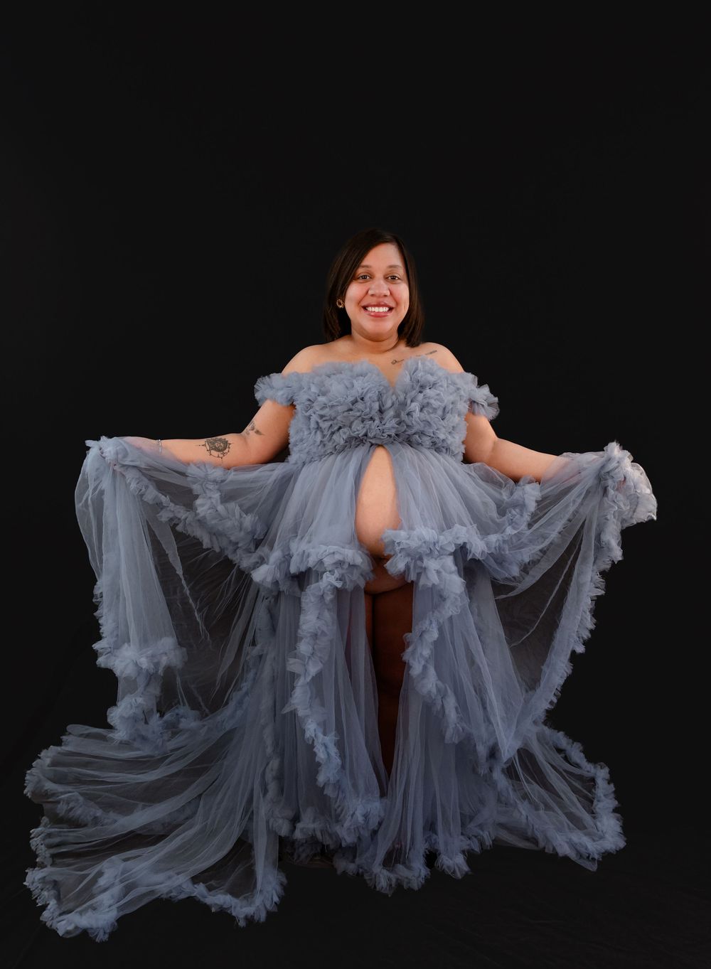 A dancer in a flowing blue-gray tulle dress performs an expressive movement sequence against a black background.