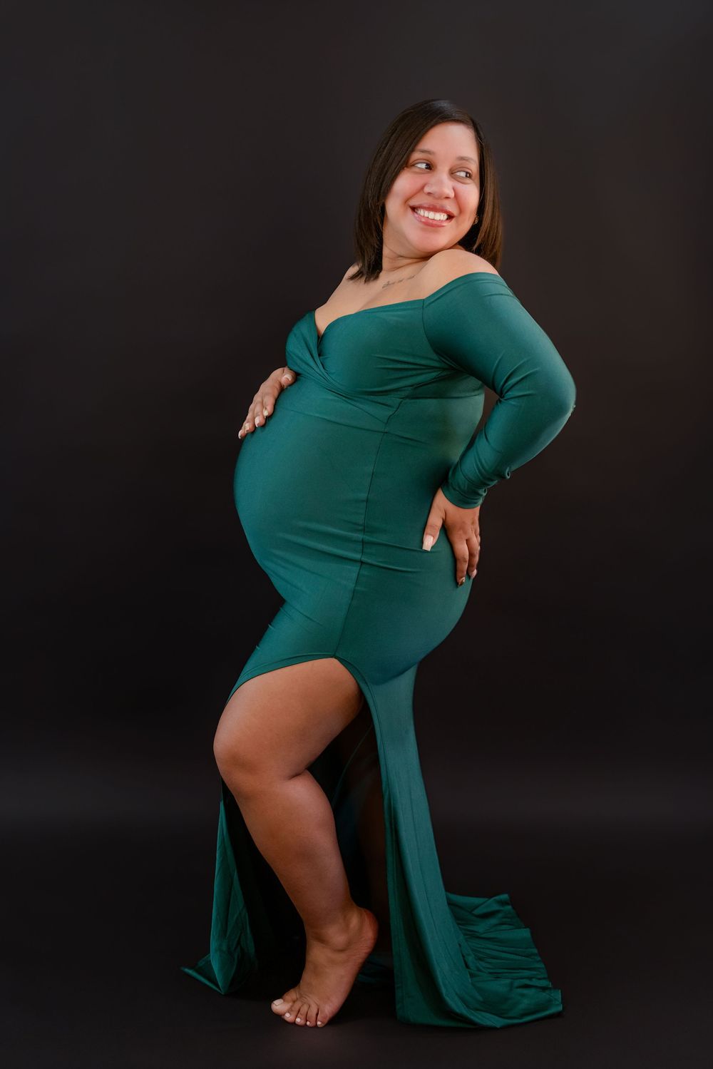 Artistic maternity photoshoot featuring a flowing emerald green dress against a dark studio backdrop.