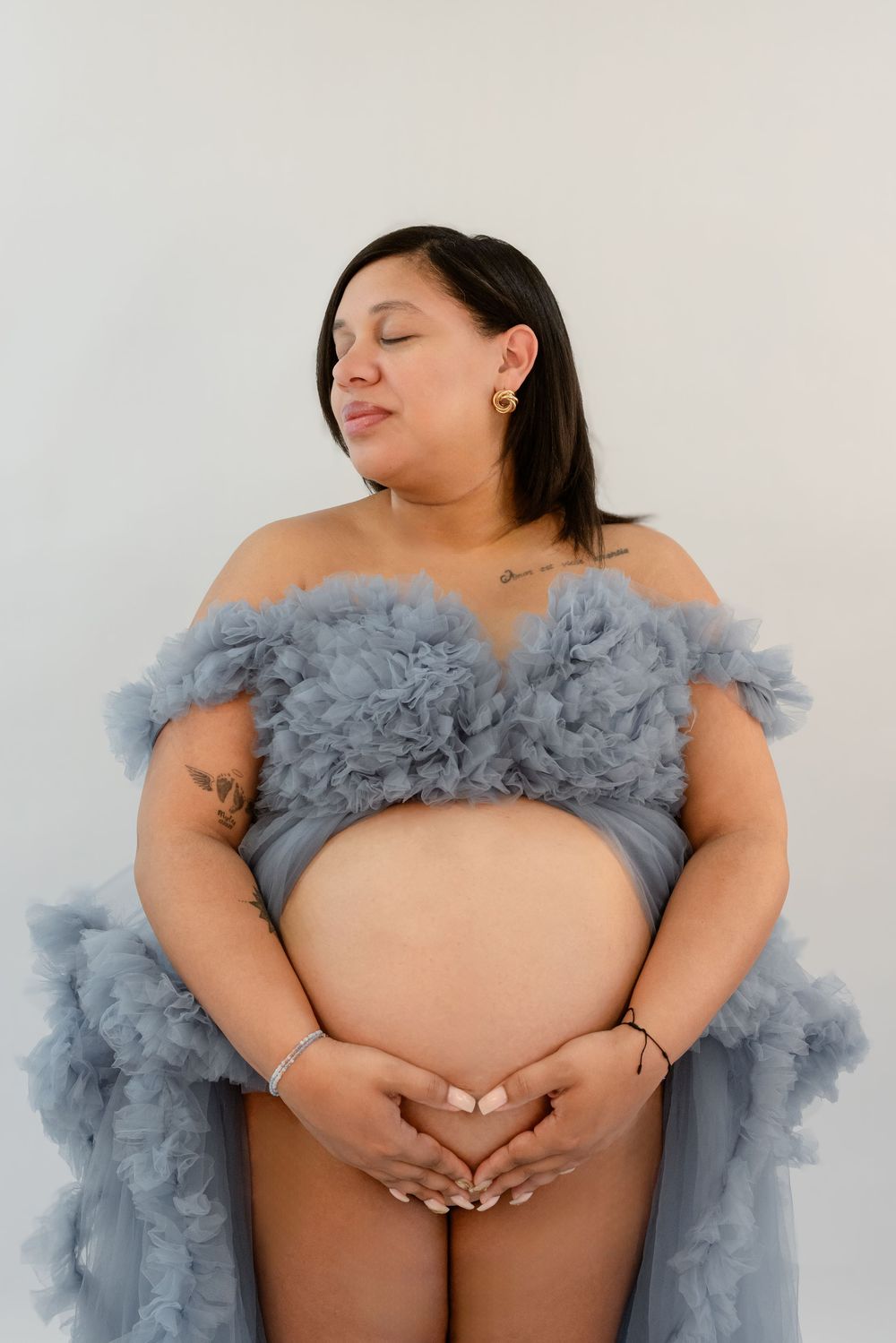 Intimate maternity photo with soft grey tulle wrap highlights expecting mother's baby bump against white backdrop.