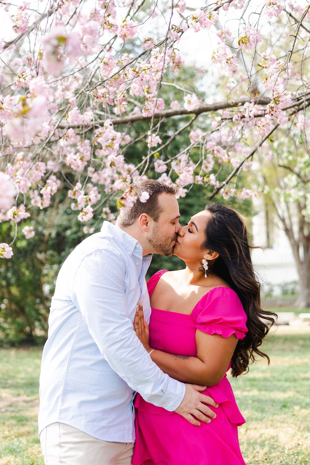Romantic couple sharing intimate moment under pink cherry blossom trees.