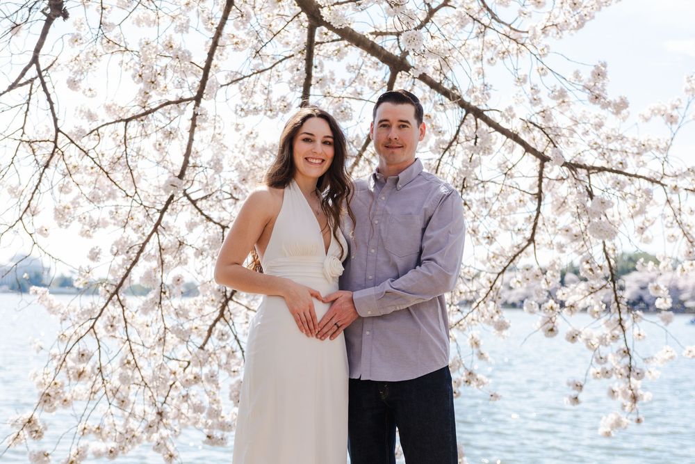 Couple embracing under blooming cherry blossom trees with water in the background.