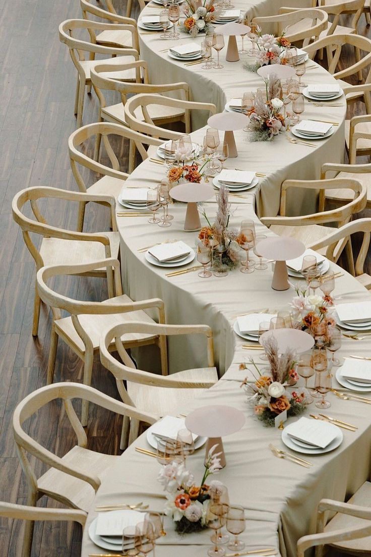 Neutral-toned wedding reception tables with wooden chairs and soft floral centerpieces.