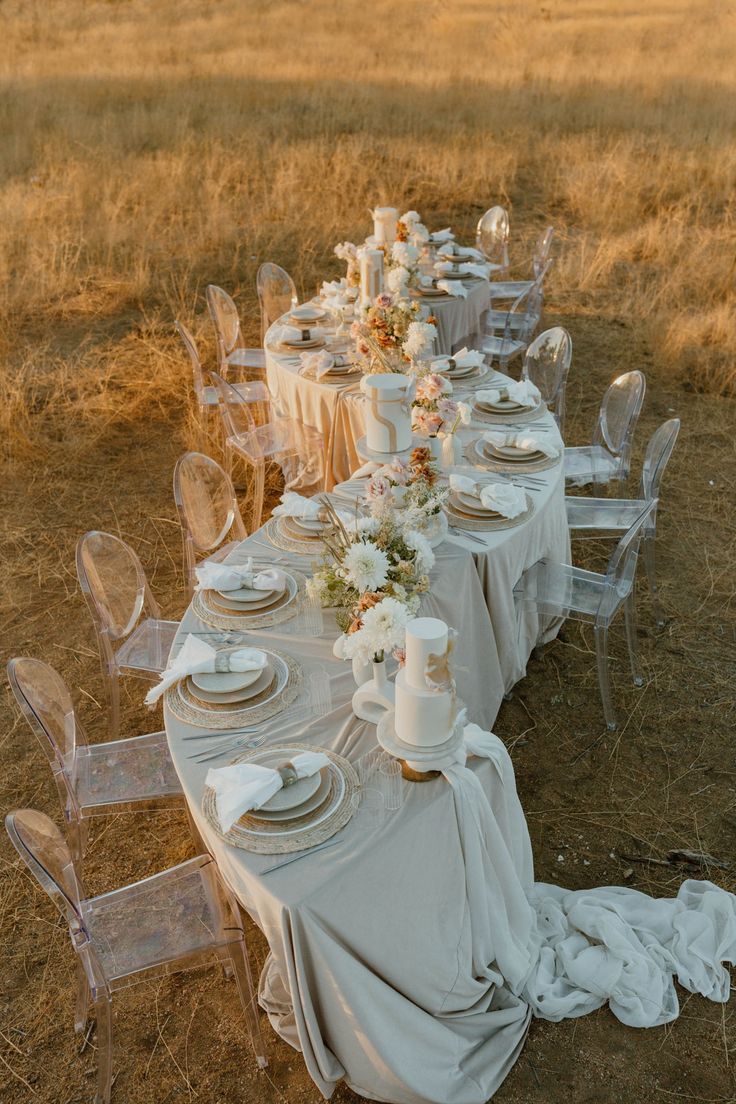 Outdoor golden hour wedding table set with ghost chairs in a dry meadow.