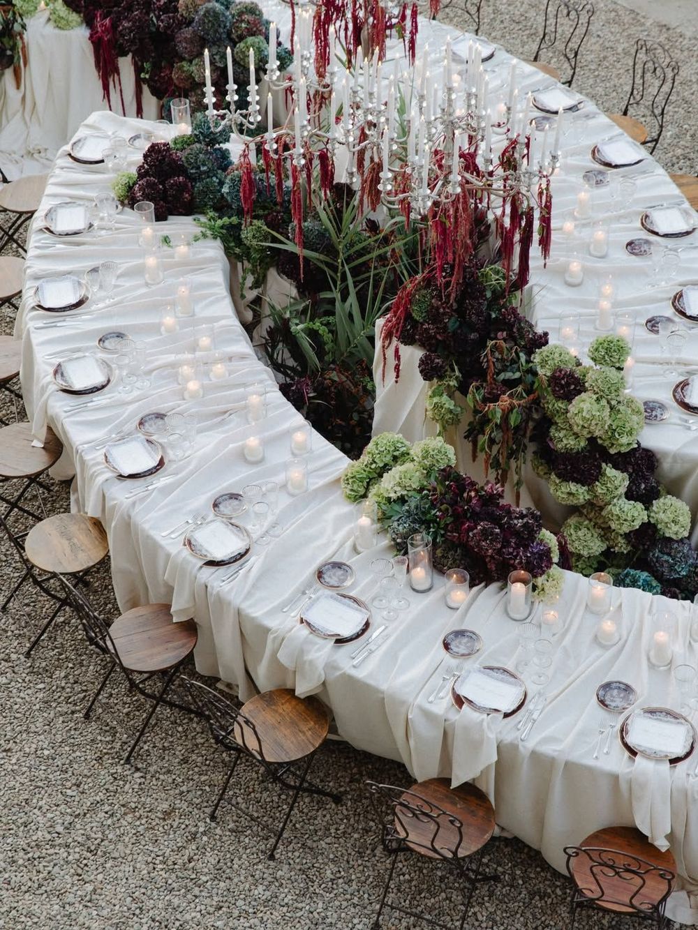 Curved wedding reception table with dark floral greenery and candlelit white linens.