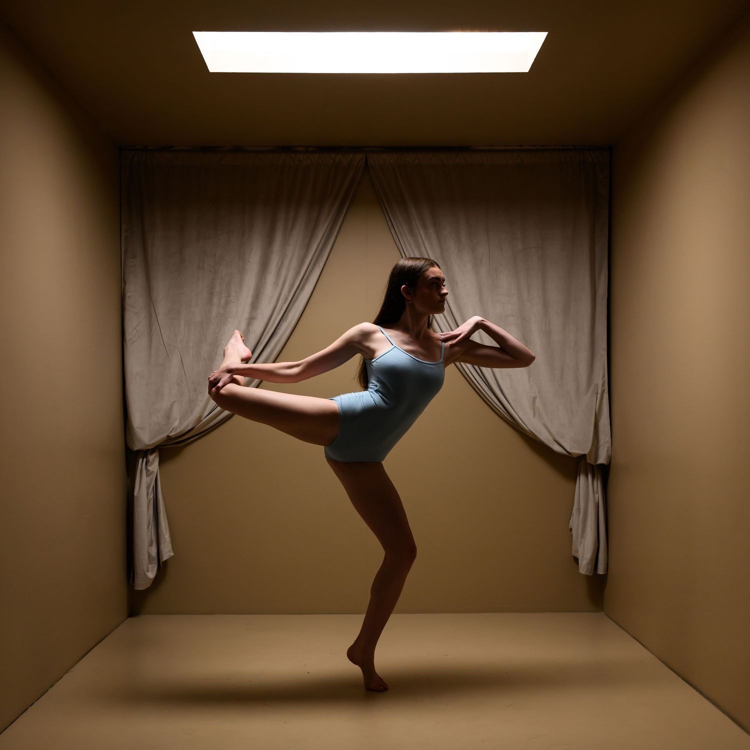 A dancer performs a graceful sequence of movements against a beige wall in a minimalist studio setting.