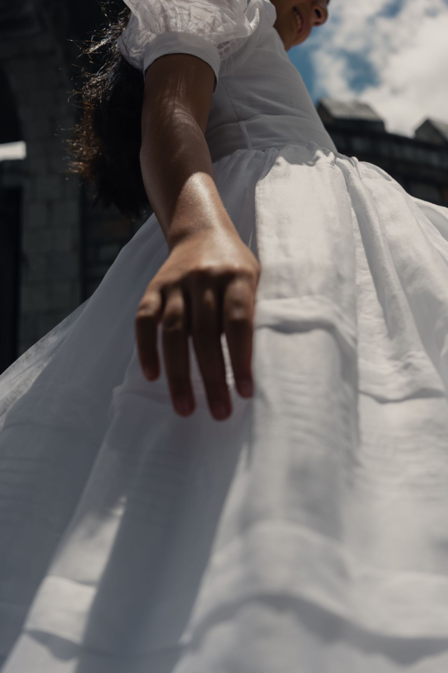 Close-up details of a flowing white wedding dress fabric against a cloudy sky background.