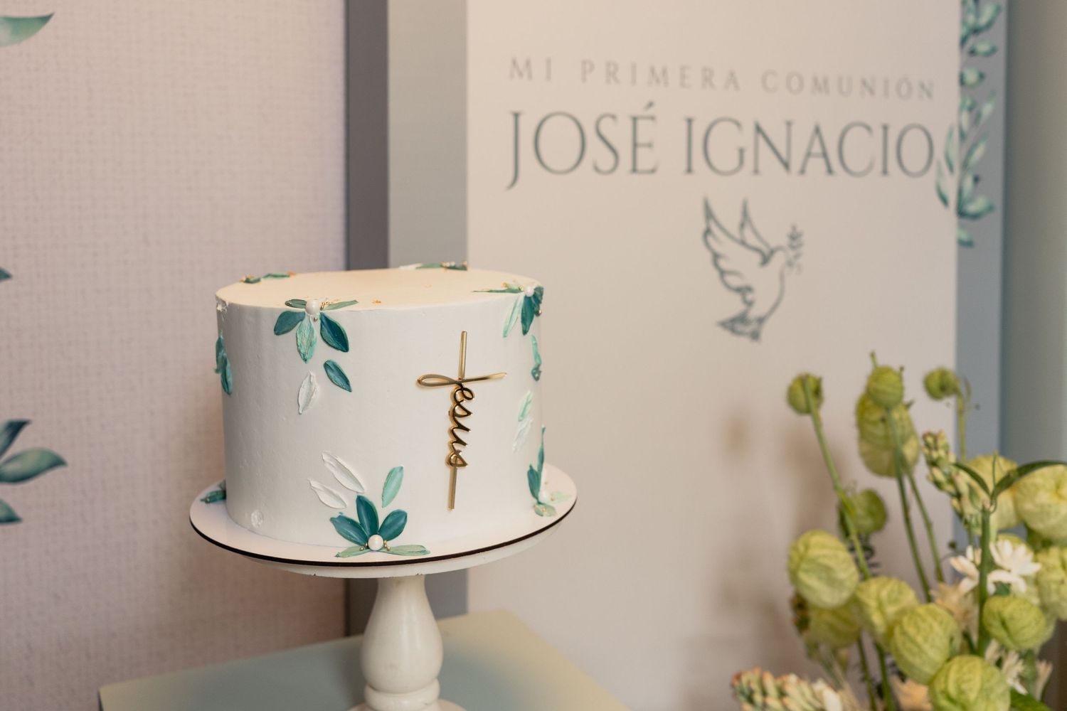 Elegant white baptism or christening cake decorated with delicate floral accents and greenery on a dessert table.