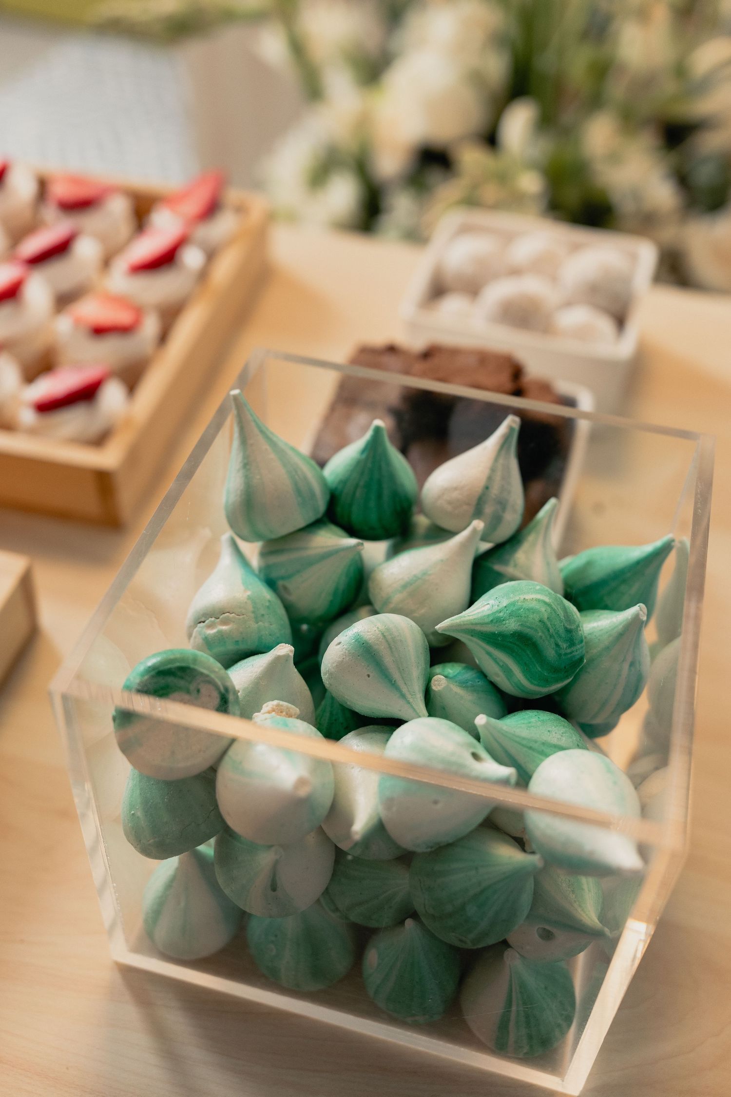 Green and white meringue kisses displayed in a clear glass container at a dessert table.