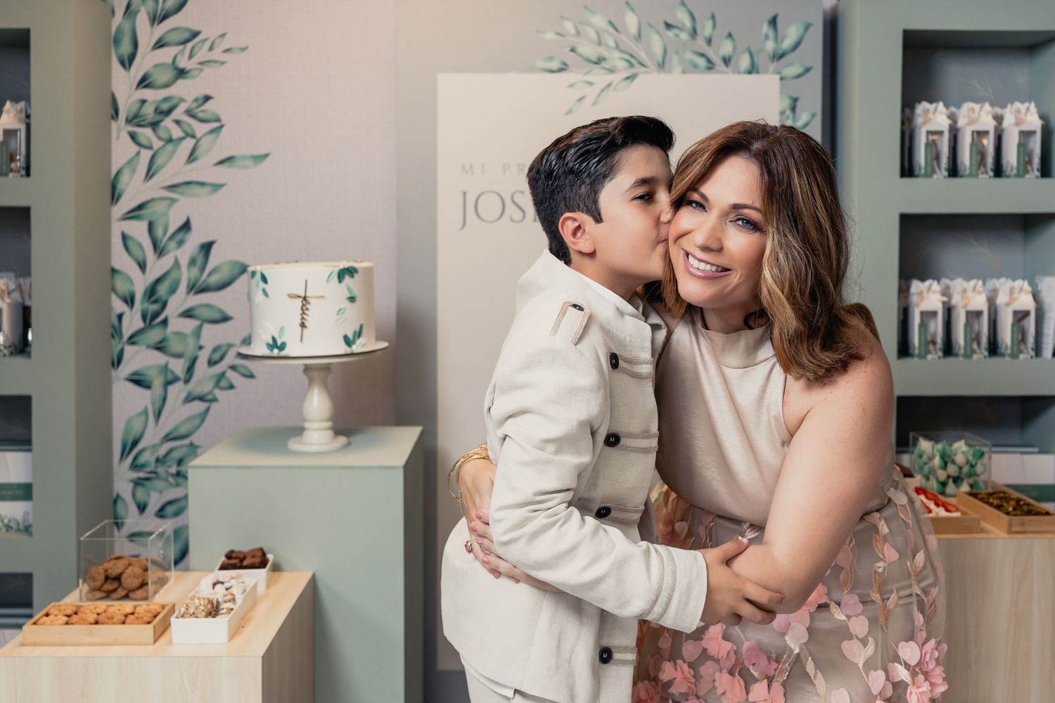 Two people embrace warmly in front of a retail display with blue decor and desserts visible in the background.