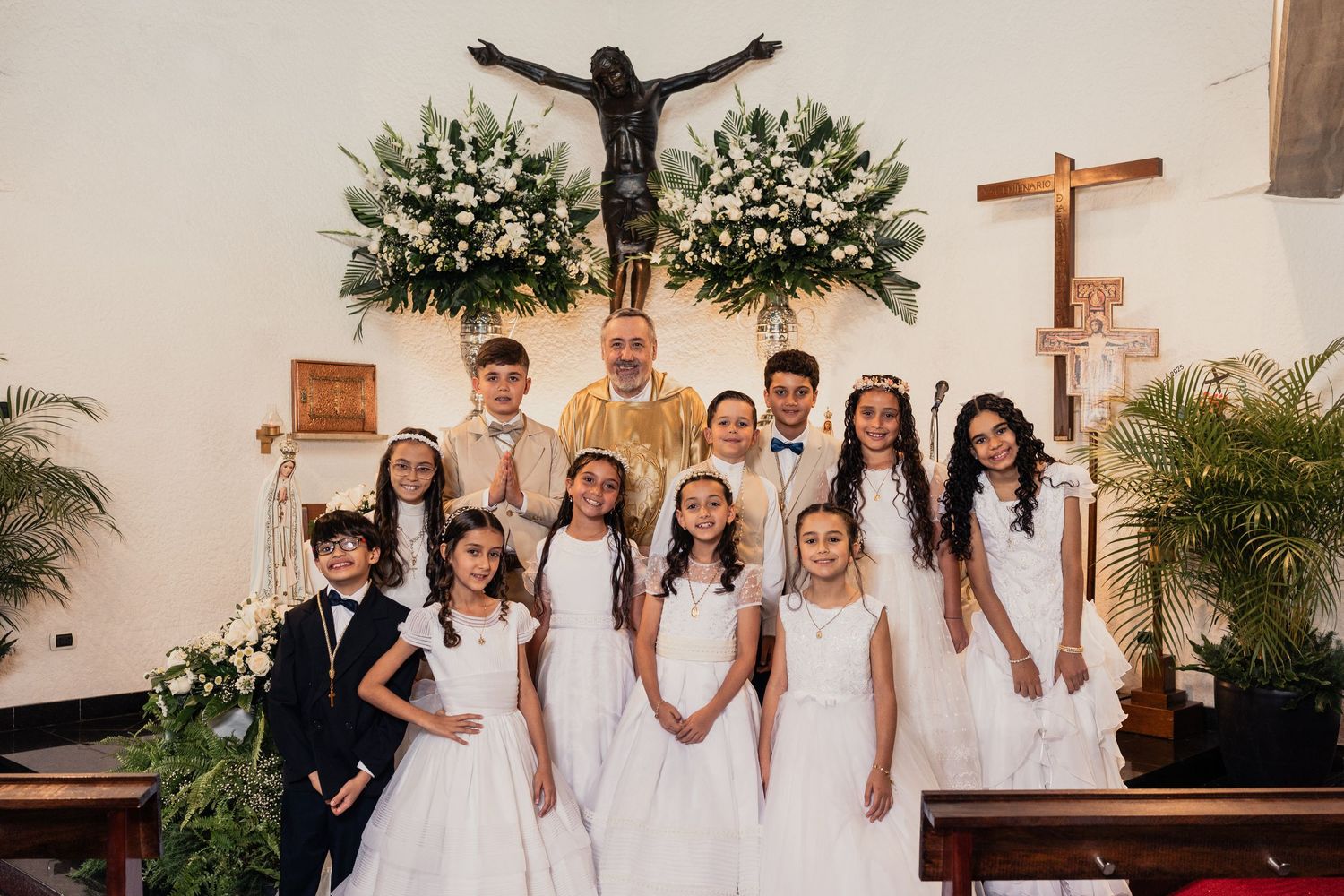 A group in white dresses and formal attire poses together for wedding party photos in a church setting.