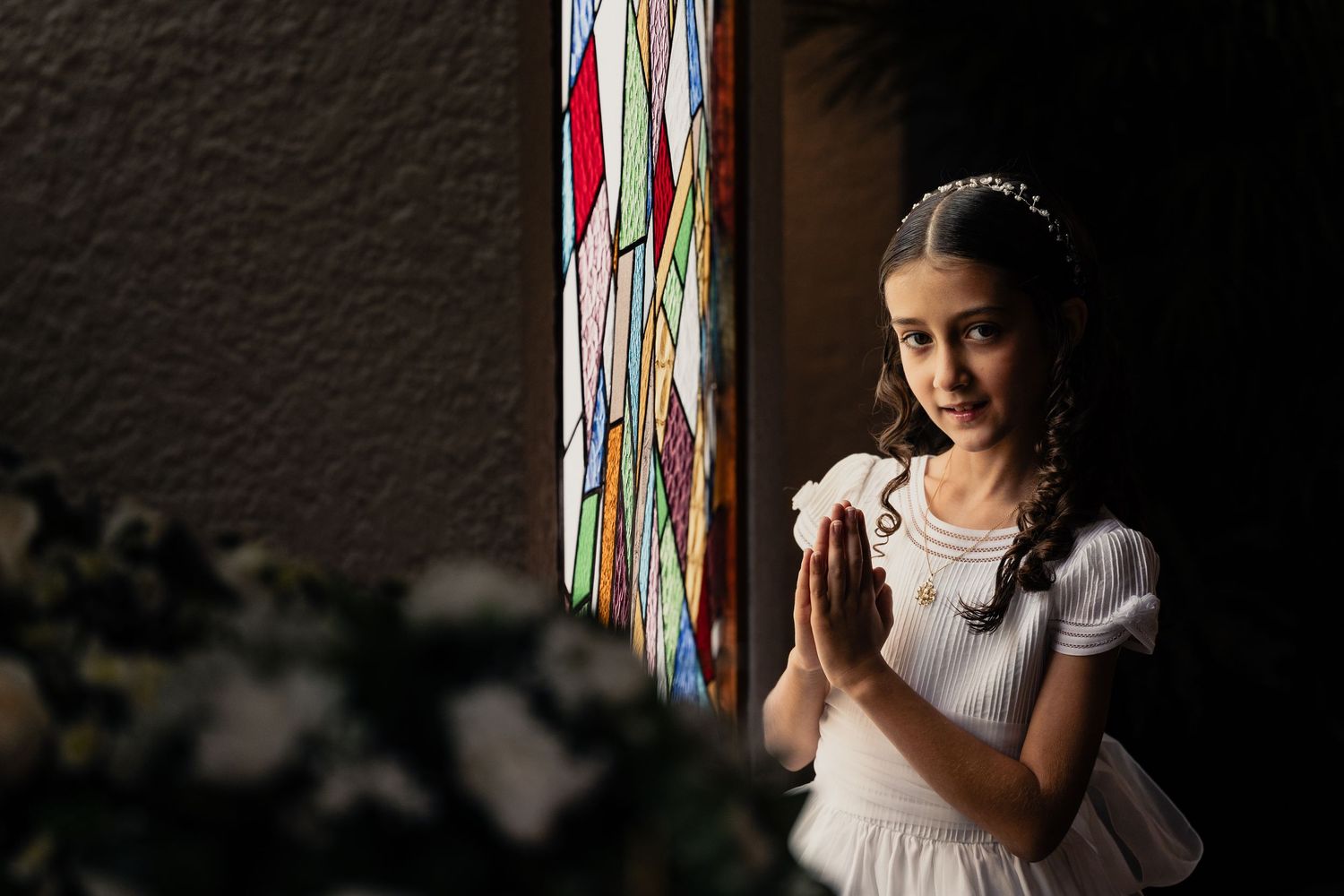 A bride in a white dress poses near colorful hanging ribbons in a dimly lit room during a wedding photoshoot.